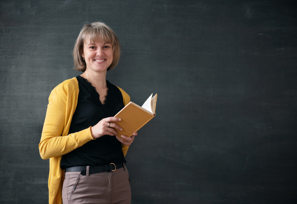 En kvindelig lærer foran tavle med en bog i hånden